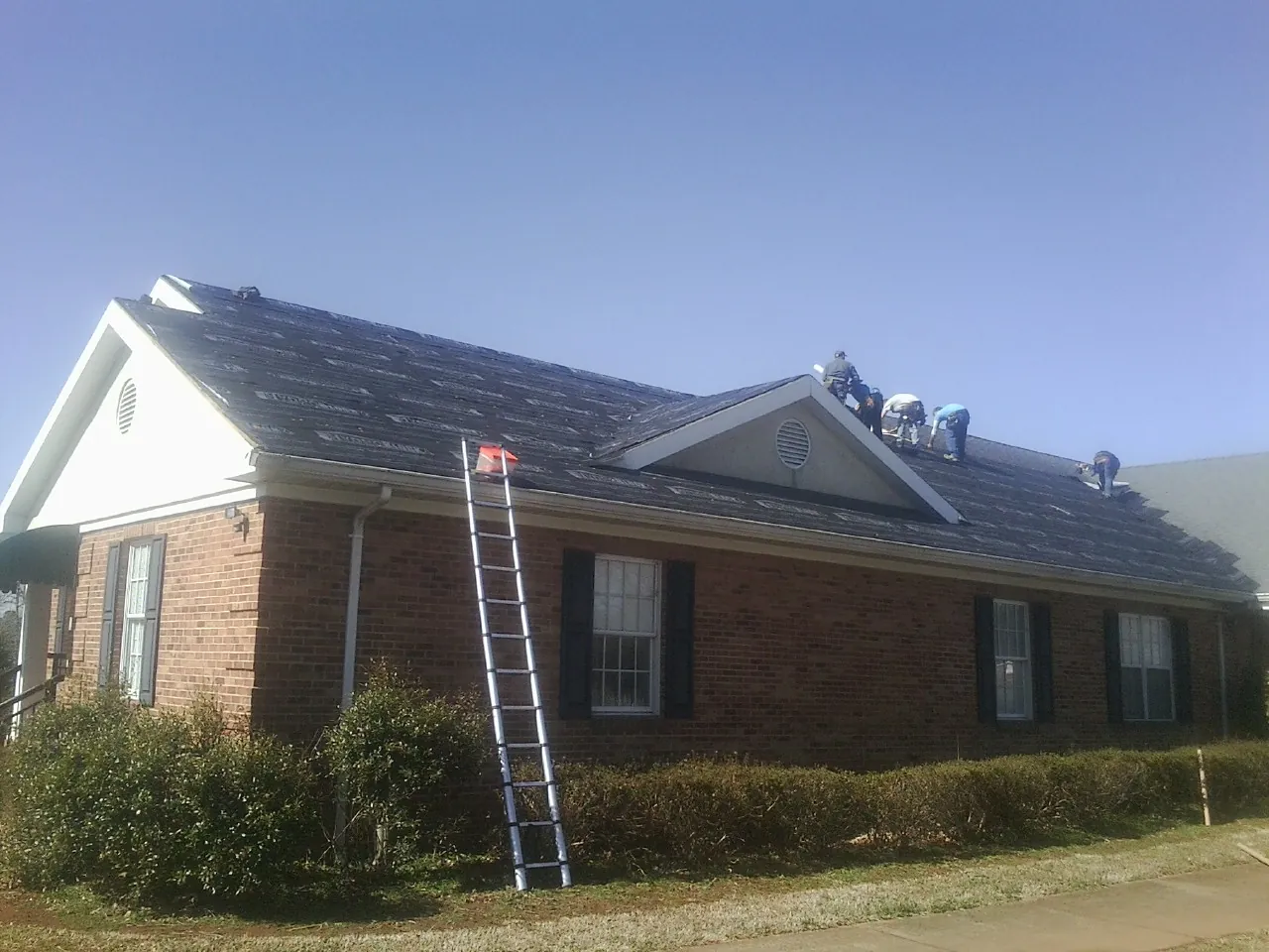 Crew tearing shingles off a brick ranch roof with a ladder set — Metal Roof Repair work by our crew in New Paltz