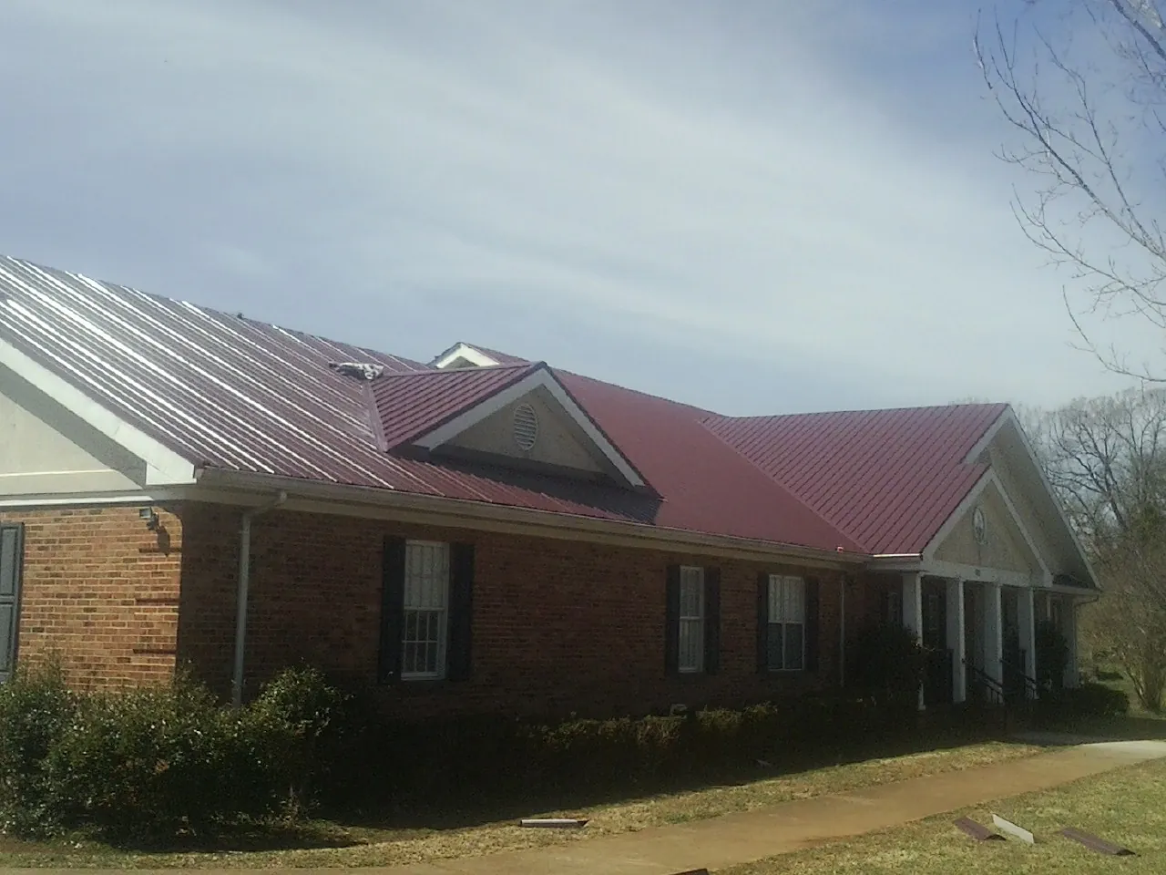 Red metal roof with gabled entries on a long brick building, from a Hail Damage Roof Repair job in New Paltz
