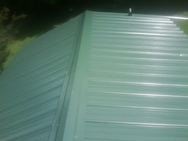 New green metal panels meeting at the ridge of a roof — Flat Roof Repair work by our crew in New Paltz
