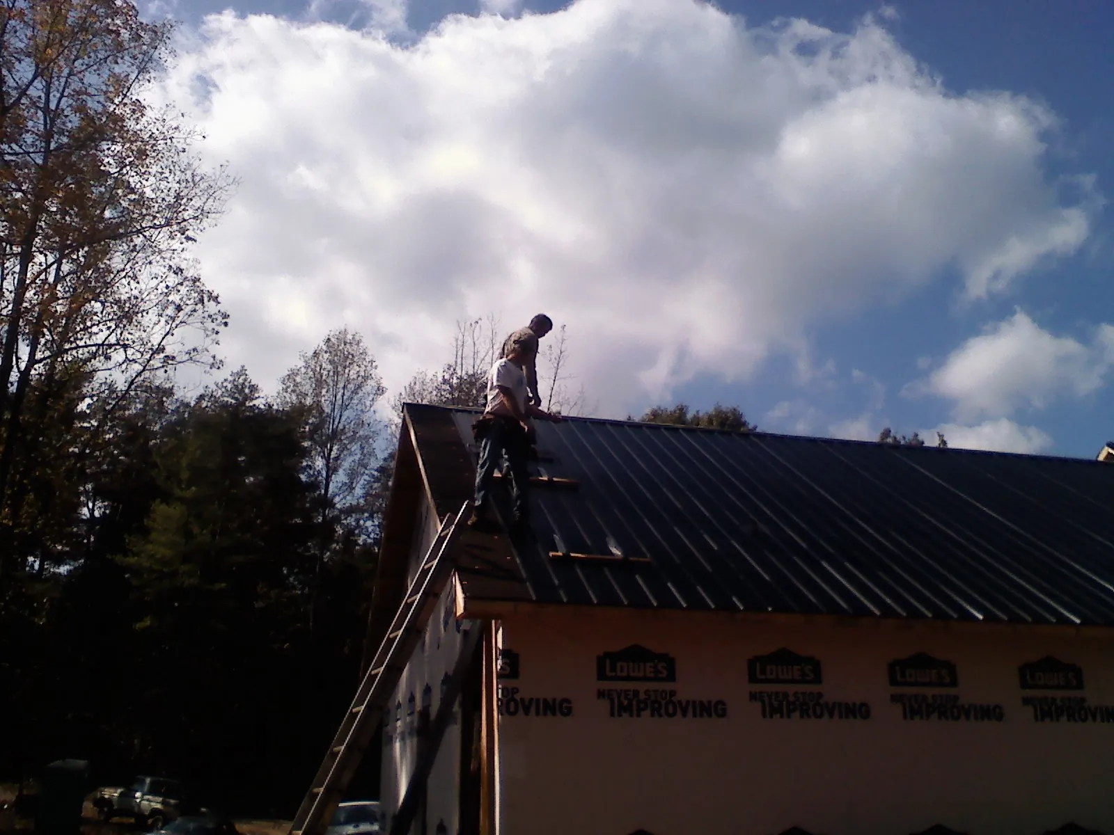 Roofer fastening dark metal panels high against a cloudy sky, from a Roof Inspection job in New Paltz