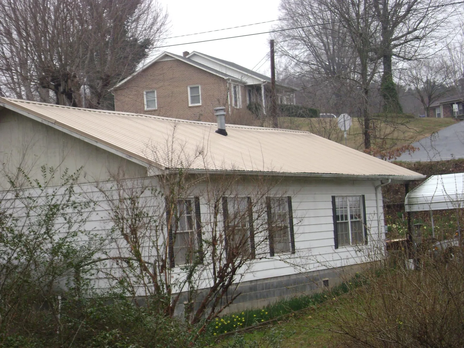 Tan metal roof on a white sided house set into a hillside — Commercial Roofing by Roofing Brothers in New Paltz